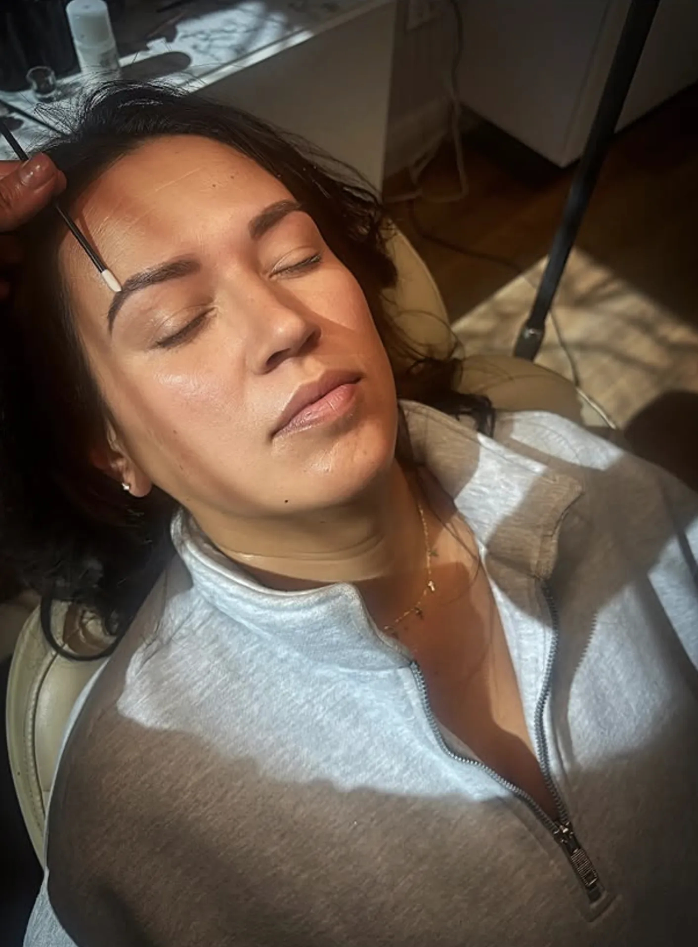 Woman receiving eyebrow treatment while relaxing in a beauty salon.