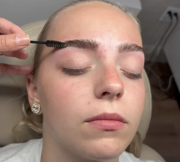 A person having their eyebrows groomed with a brush in a salon setting.